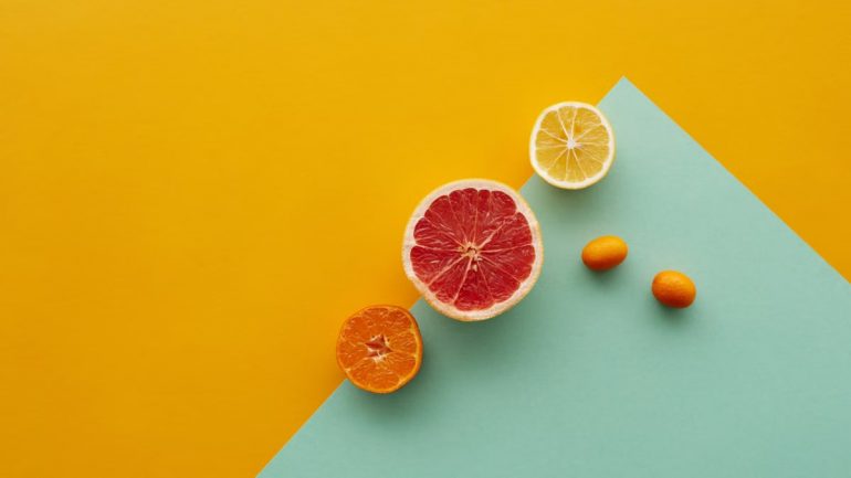 Creative display of sliced citrus fruits on a yellow and teal background showcasing fresh and vibrant colors.